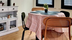 A dining area with a table set for two, a white cabinet with storage, and a window with a view of greenery outside. - Cobalt - Casa do Parque (Aveiro)