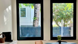 A room with two windows, a table with a pink tablecloth, a chair, a white cabinet, and a wooden floor. - Cobalt - Casa do Parque (Aveiro)