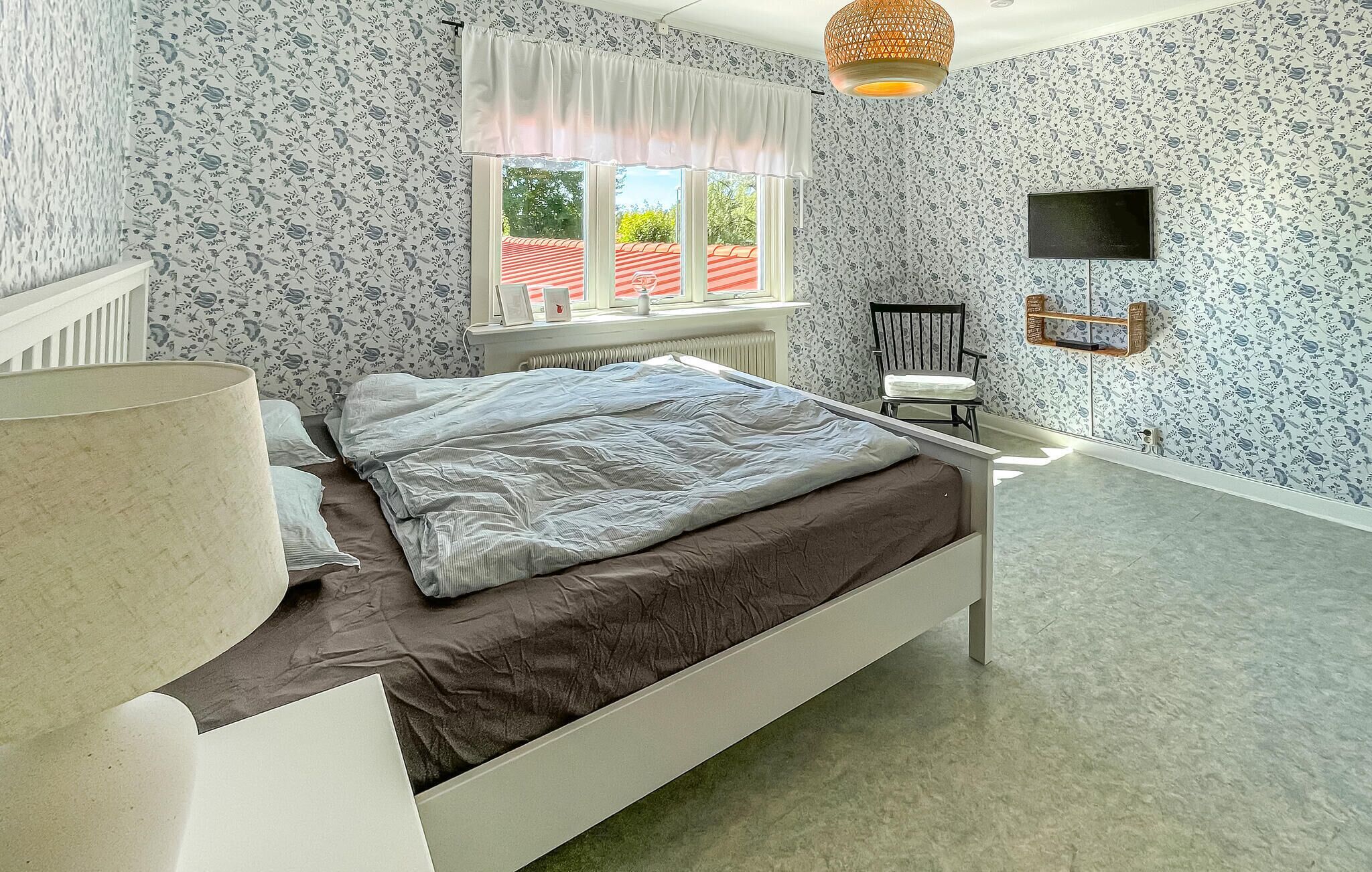 A bedroom with a bed, a chair, a TV, and a window with a view of a red-roofed building.