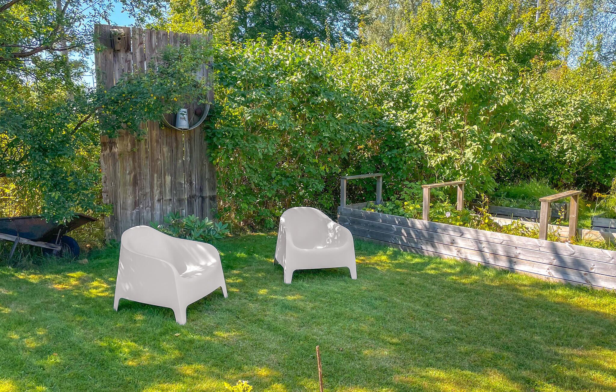 Un jardin avec deux chaises blanches, une clôture en bois et un arbre sur lequel est accrochée une nichoir.