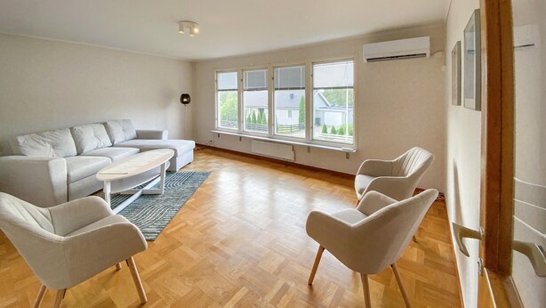A modern living room with a sofa, two armchairs, and a coffee table. Large windows provide natural light and a view of the outside. - Beautiful apartment in Pauliström (Pauliström)