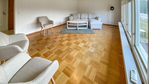 A spacious living room with a wooden parquet floor, a white sofa, a round coffee table, and a grey armchair. - Beautiful apartment in Pauliström (Pauliström)