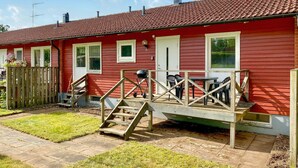 A red house with a tiled roof, a wooden deck, and a small outdoor seating area. - Beautiful apartment in Pauliström (Pauliström)