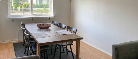A dining area with a wooden table, black chairs, a woven basket, and a window with a view of greenery.
