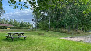 Ein Picknicktisch in einer grünen Umgebung mit Bäumen und einer Bank im Hintergrund.