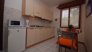 Cocina compacta con microondas, cafetera y una mesa de comedor con una silla.