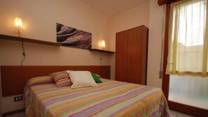 Un dormitorio con cama, un armario de madera, una repisa con un cuadro y una ventana con cortinas.