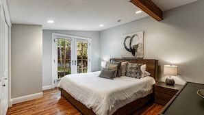 Un dormitorio con cama de madera, mesita de noche, lámpara y un cuadro en la pared.