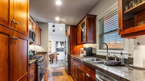 Una cocina con armarios de madera, electrodomésticos de acero inoxidable, encimera de granito y una ventana con persianas.