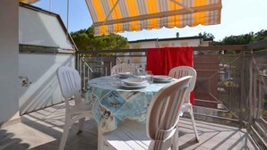An outdoor patio with a table set for dining, surrounded by chairs, under a striped awning.