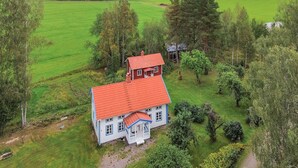 A two-story house with a red roof, surrounded by green fields and trees. - Beautiful home in Gunnarsbytorp with sauna (Gunnarsbytorp)
