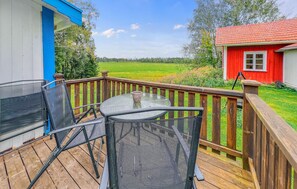 Une terrasse en bois avec une table et des chaises, donnant sur un champ verdoyant et un bâtiment rouge.