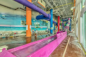An indoor water park with slides, a pool, and a mural of a beach scene.