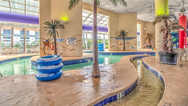 Una piscina interior con un cartel de salvavidas, palmeras y un mural en la pared.