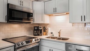 A modern kitchen with white cabinetry, a stainless steel range, a built-in oven, a coffee maker, and a double sink. - Ocean Forest Villas C-114 (Myrtle Beach)