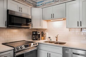 Una cucina moderna con mobili bianchi, piano cottura in acciaio inossidabile, forno integrato, macchina per caffè e lavello a due vasche.