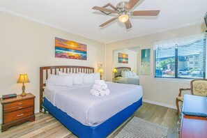 A bedroom with a bed, bedside lamps, a ceiling fan, a window with blinds, and artwork on the walls. - Ocean Forest Villas C-114 (Myrtle Beach)