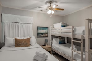 Una habitación de hotel con cama, mesita de noche, ventilador de techo y literas.