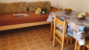 A room with a sofa, a dining table with chairs, a flat-screen TV mounted on the wall, and a framed picture.