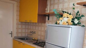 A compact kitchen with yellow cabinets, a stainless steel refrigerator, and a decorative plant on the counter.