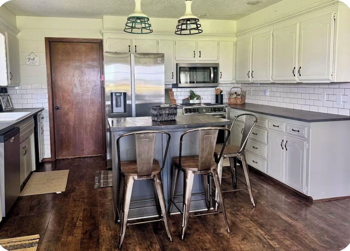 A kitchen with white cabinets, a wooden door, and a central island with bar stools.