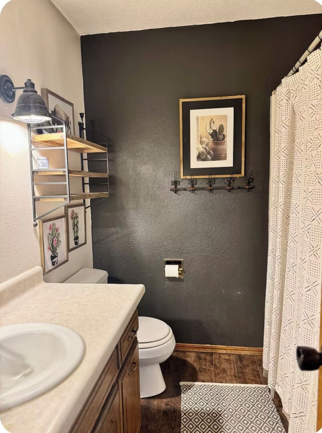 Et badeværelse med en mørk væg, toilet, vask med spejl og badeforhæng.