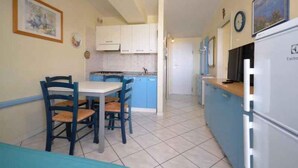 Cocina compacta con zona de comedor, que incluye una mesa con sillas, un refrigerador y armarios.