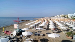 Una playa con filas de sombrillas blancas y sillas de tomar el sol, una torre de salvavidas y edificios al fondo.