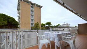 Una terraza con una mesa y sillas, barandilla blanca y un edificio al fondo.