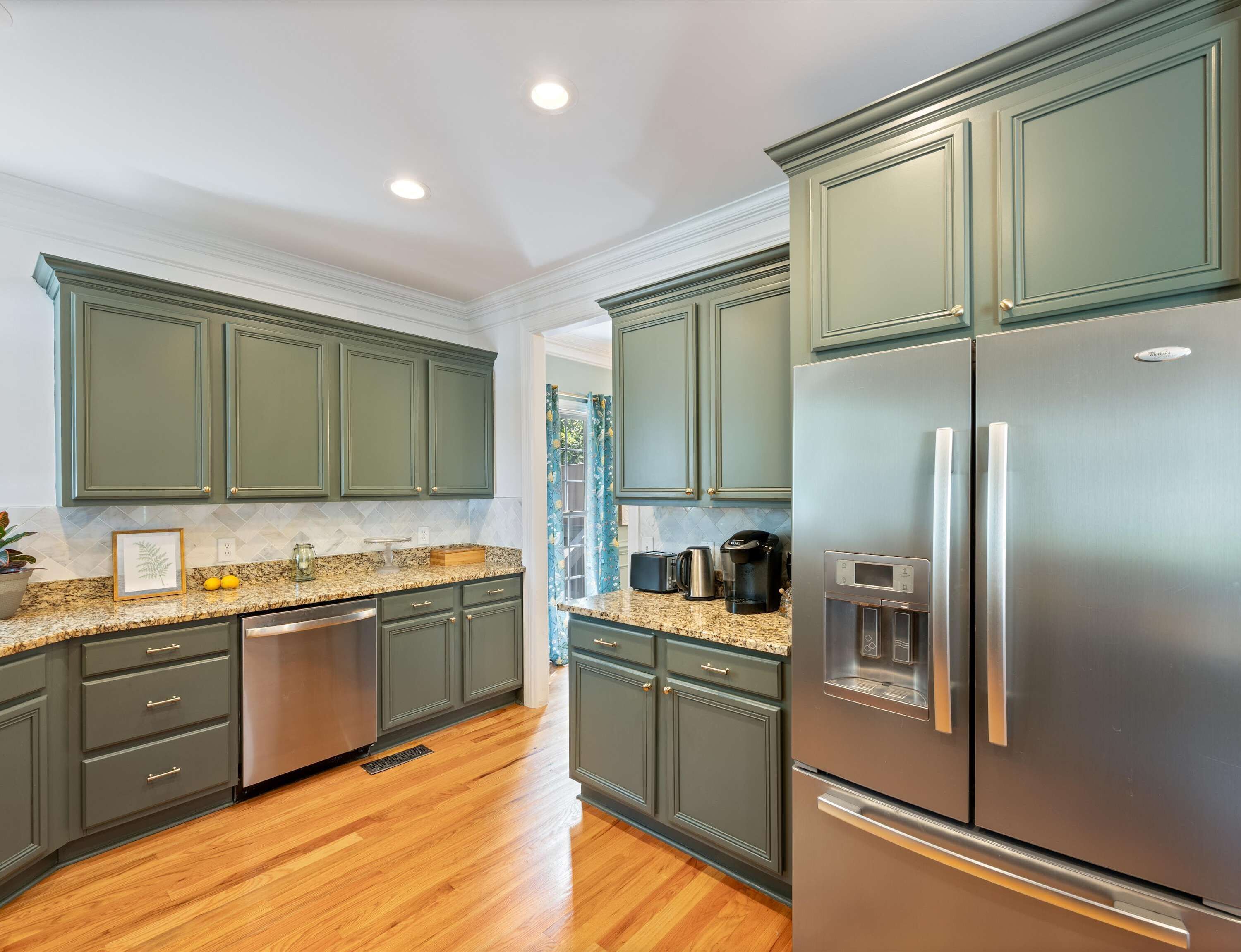 A modern kitchen with dark green cabinets, stainless steel appliances, and a granite countertop.