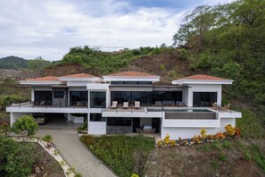 A modern two-story house with a flat roof, large windows, and a patio area.