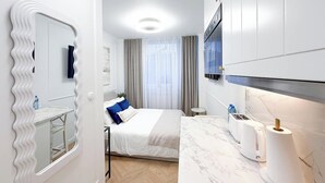 Et moderne hotelværelse med seng, badeværelse med spejl, håndvask og et tekøkken med brødrister og elkedel.