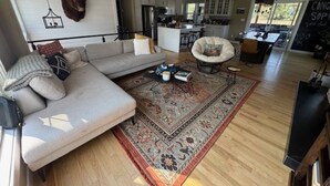 A modern living room with a large sofa, a coffee table, and a decorative rug. There is a kitchen area visible in the background.