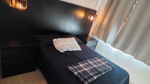 Una camera da letto moderna con una testata scura, un comodino nero, un letto con coperta a quadri e due luci fissate alla parete.