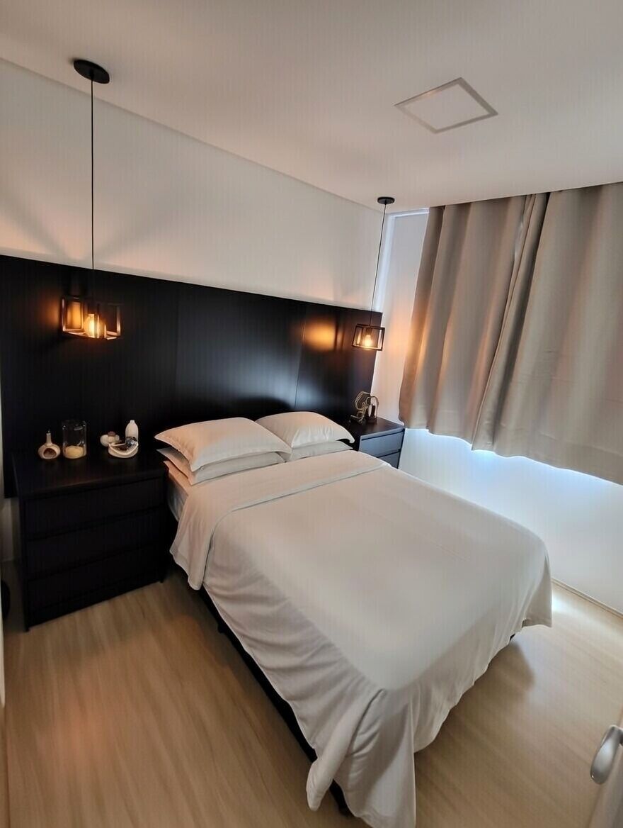 Moderni hotellihuone, jossa on suuri sänky, tumma pääty, yöp öytävalaisimet ja ikkuna, jossa on verhot.