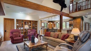 A spacious living room with a high ceiling, wooden beams, a fireplace, a large sofa, two armchairs, a coffee table, and a bookshelf. - Streamside Lane: Riverside Frisco Home, Dog Friendly, Near Slopes (Frisco)