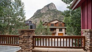 A wooden deck with a stone pillar, a view of a mountain, and a building with a red exterior. - Streamside Lane: Riverside Frisco Home, Dog Friendly, Near Slopes (Frisco)