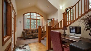 A spacious living area with a wooden staircase, a large window, a sofa, a desk with a computer, and a decorative rug. - Streamside Lane: Riverside Frisco Home, Dog Friendly, Near Slopes (Frisco)