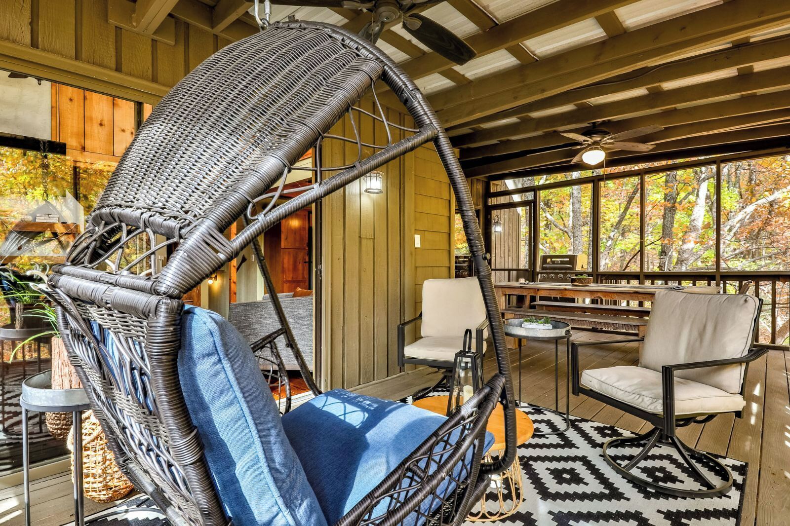 A cozy indoor space with a hanging chair, a dining area, and a large window offering a view of trees.