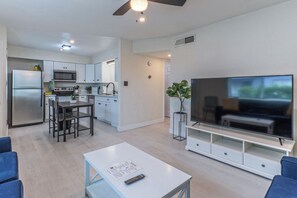 Une cuisine moderne équipée d’un réfrigérateur, d’un four à micro-ondes et d’une cuisinière, un coin repas avec des chaises, une table blanche et un téléviseur à écran plat posé sur un meuble.
