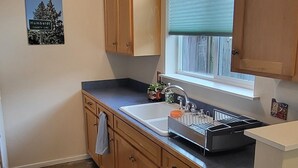 A kitchen with wooden cabinets, a window with blinds, a countertop with a coffee maker, and a rug on the floor. - Arcata Sunset Townhouse (Arcata)