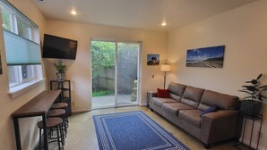 A living room with a sofa, a coffee table, a TV, and a sliding glass door leading to a garden. - Arcata Sunset Townhouse (Arcata)