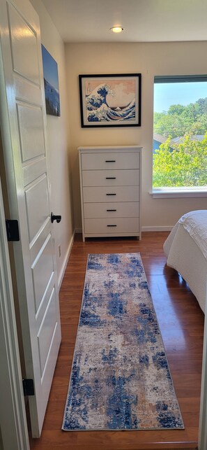 A bedroom with a bed, a dresser, a rug, and a window with a view.