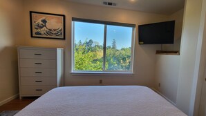 A bedroom with a large window, a bed, a dresser, and a mounted TV. - Arcata Sunset Townhouse (Arcata)