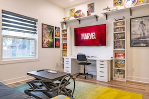 A room with a desk, chair, and a large wall-mounted TV displaying the Marvel logo.