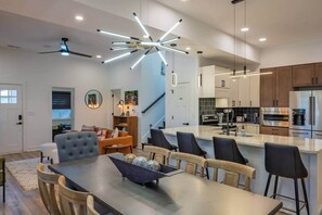 A modern kitchen with stainless steel appliances, a dining area with a large table and chairs, and a living room with a sofa and a coffee table.