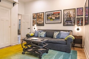 A living room with a grey sofa, a coffee table, and framed movie posters on the wall.