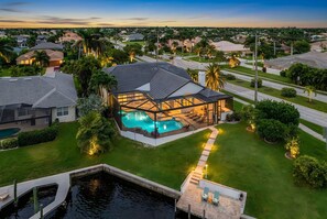 A modern house with a swimming pool, surrounded by well-maintained lawns and palm trees. - Riverfront Luxury with Heated Pool, Spa & Private Dock – Sunny Shores Escape (Cape Coral)
