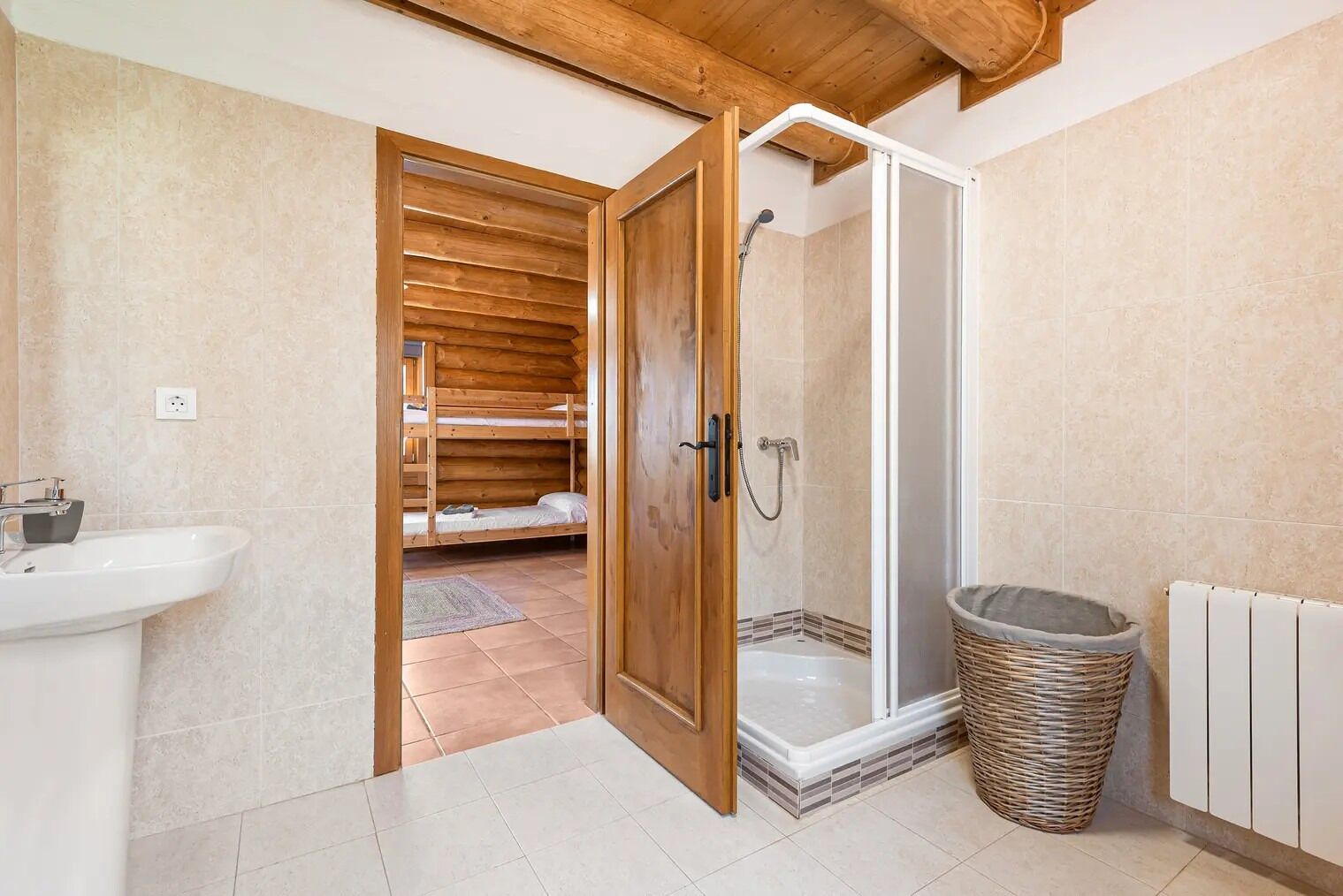 Une salle de bain avec une cabine de douche en bois, un lavabo et un petit panier en osier.