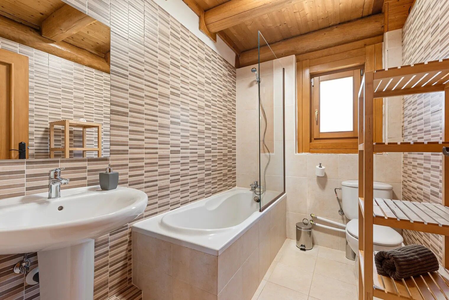 A bathroom with a sink, bathtub, and toilet, featuring wooden beams and tiled walls.